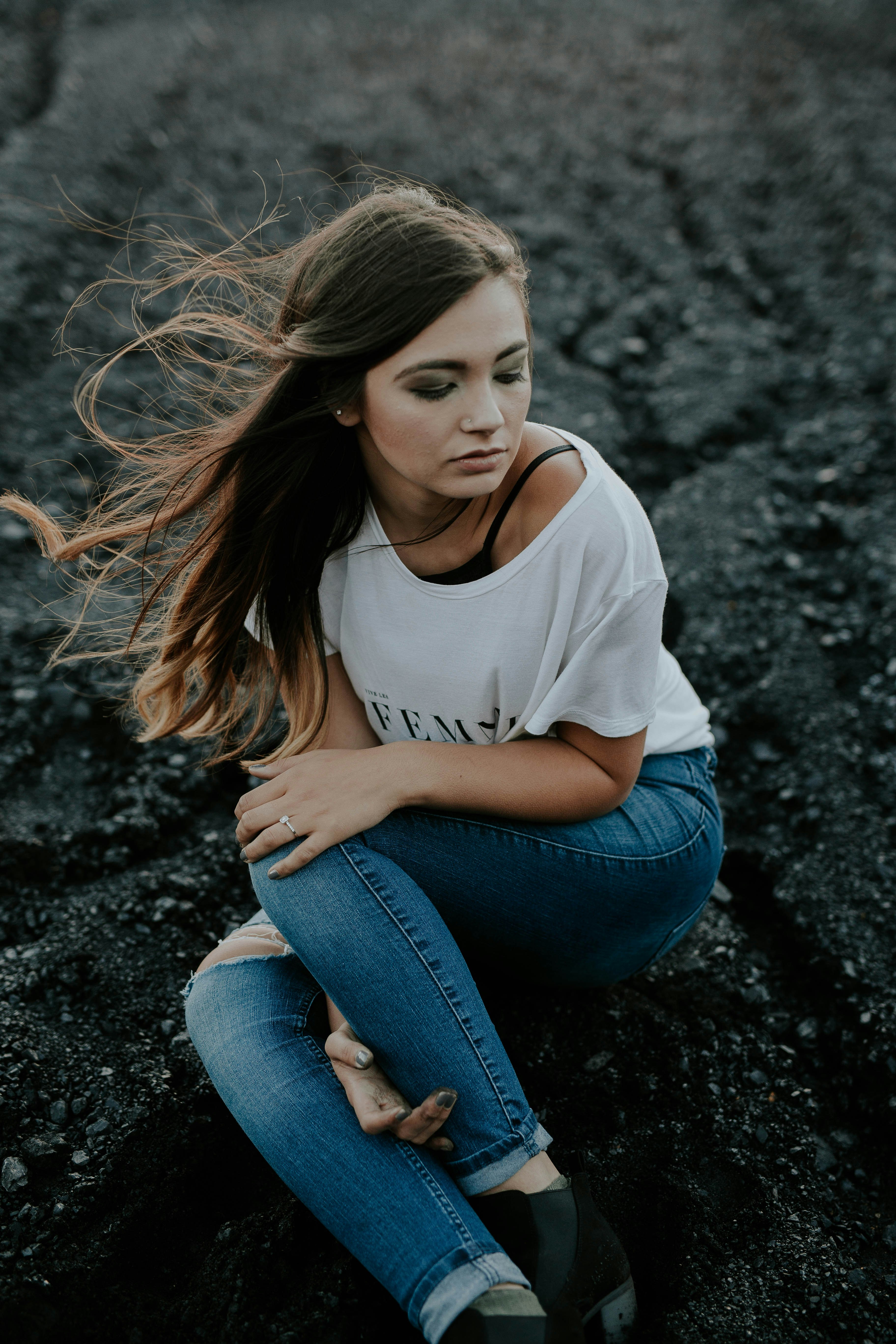 woman wearing scoop-neck shirt and distressed jeans sitting on ground while holding knee